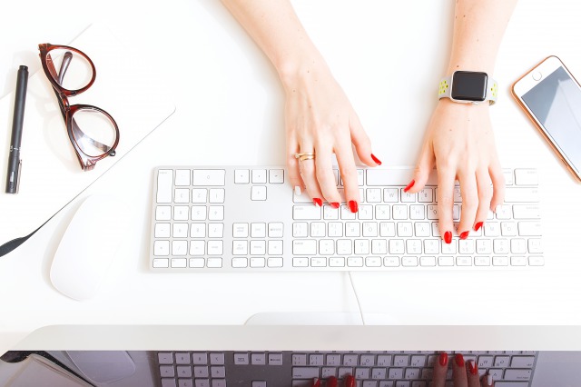 パソコンを使う赤いネイルカラーの女性の手もと